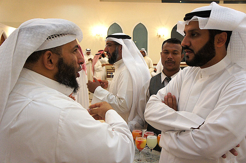 several men in white tuxedos are talking at a party