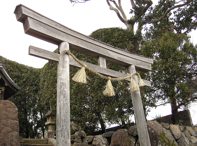 a large asian shrine with a long wooden fence and grass hanging from it's side