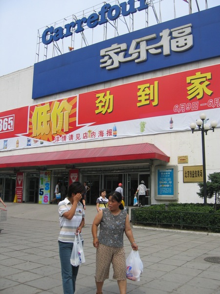 two ladies walk past the front of a building with many stores in it