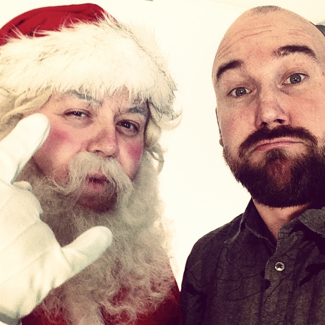 a bearded man in santa claus outfit standing next to a bald man