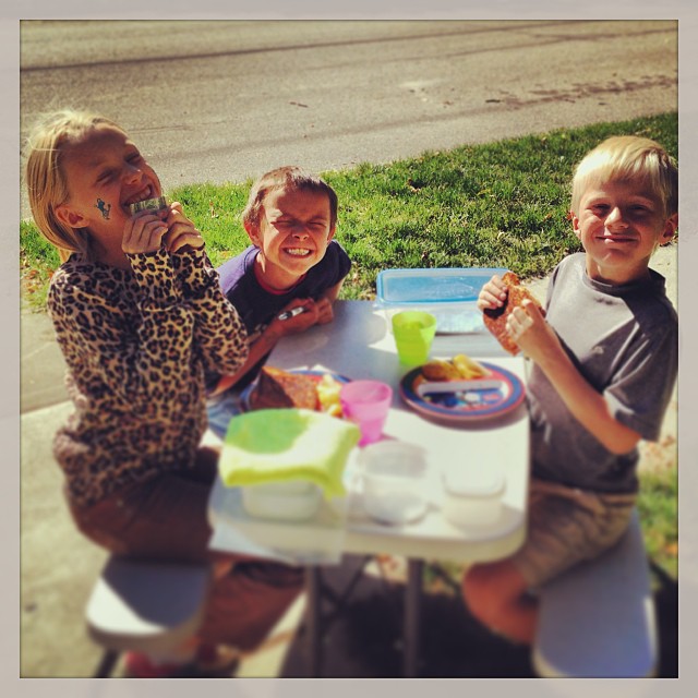 three children at an outdoor table sharing their lunch