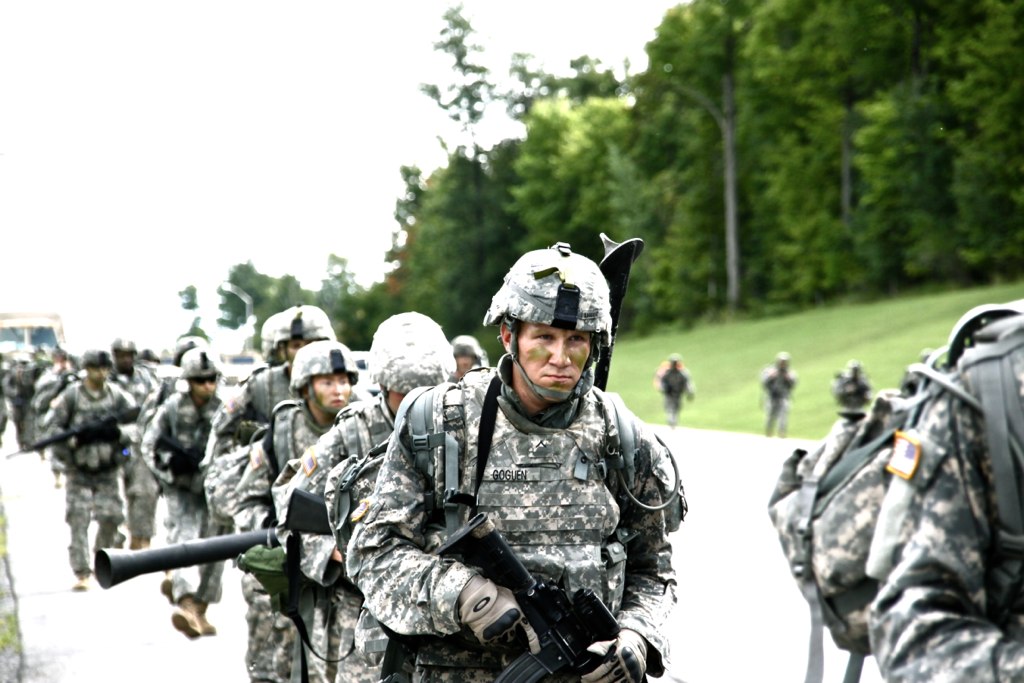 military men with weapons are walking down the road