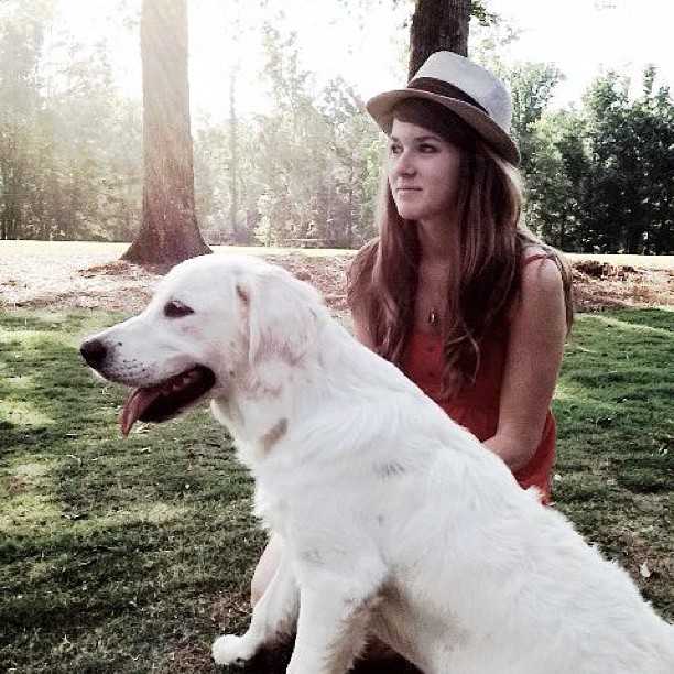 a person in a hat sits with a white dog