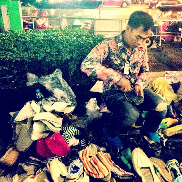 a man sits on a pile of shoes as he talks on the phone