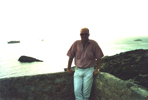 the man is standing on the edge of a rock wall looking towards water