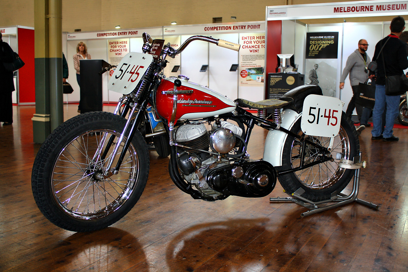 a motorcycle sits in a museum as a group of people walk by