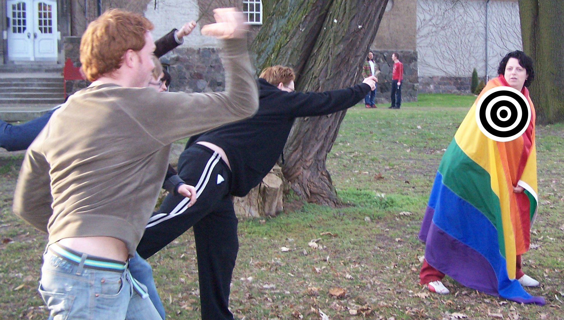 two men holding a cell phone are next to a person wearing a rainbow dress