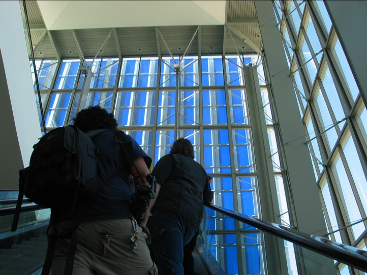 several people climbing up and down a very tall glass and metal staircase