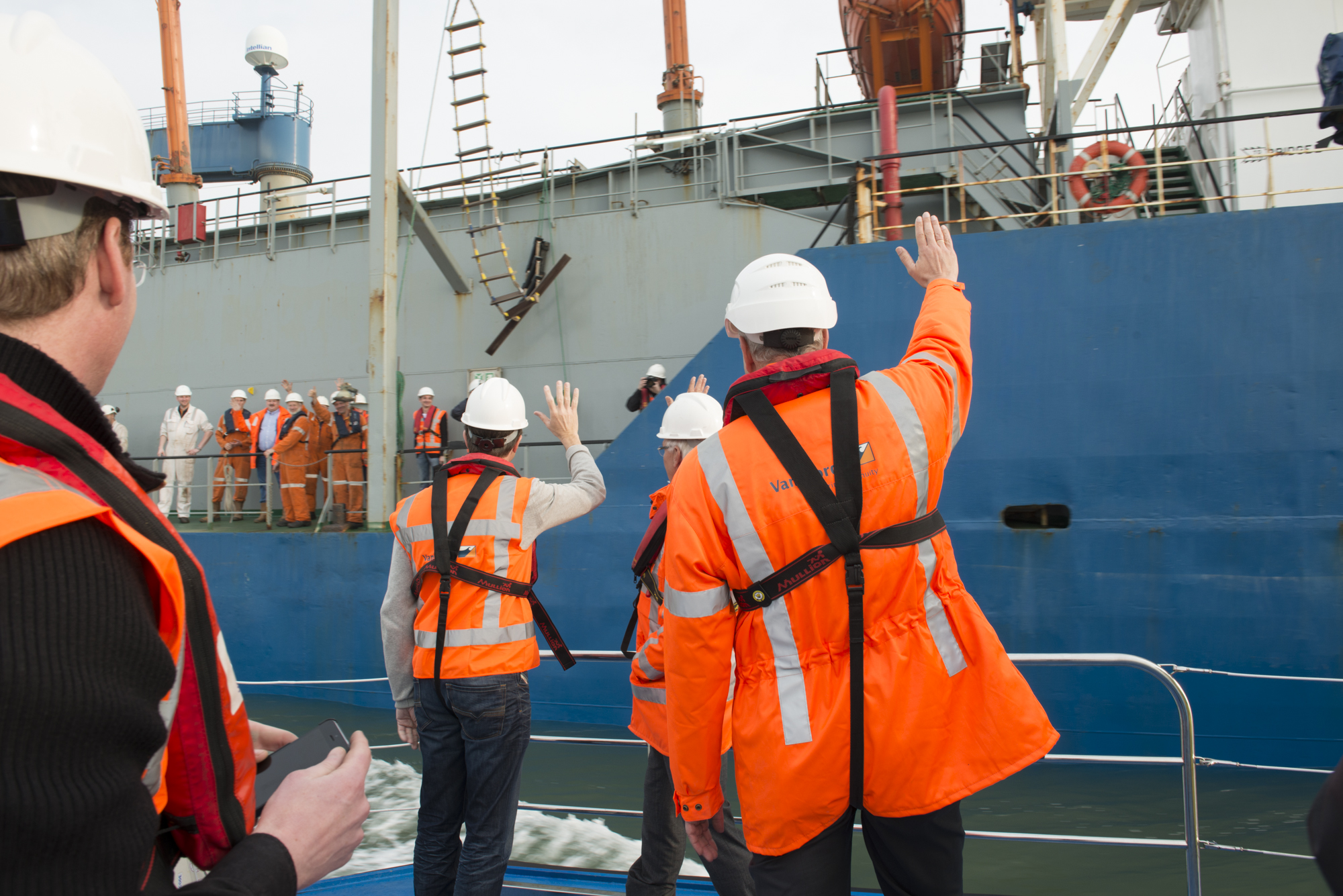 there are men in jackets and vests waving to the boat