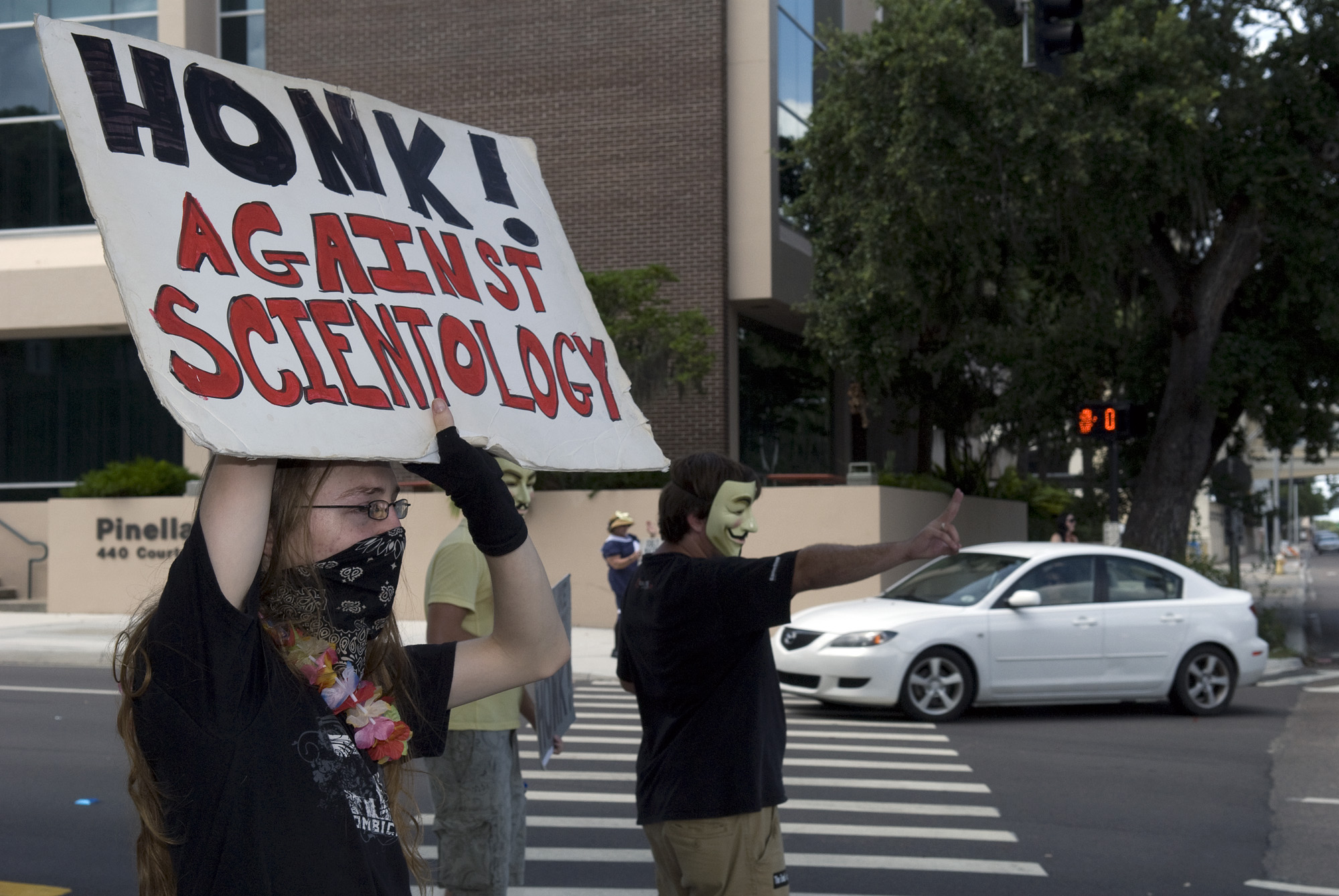 a person holding up a sign saying, honk against scientology