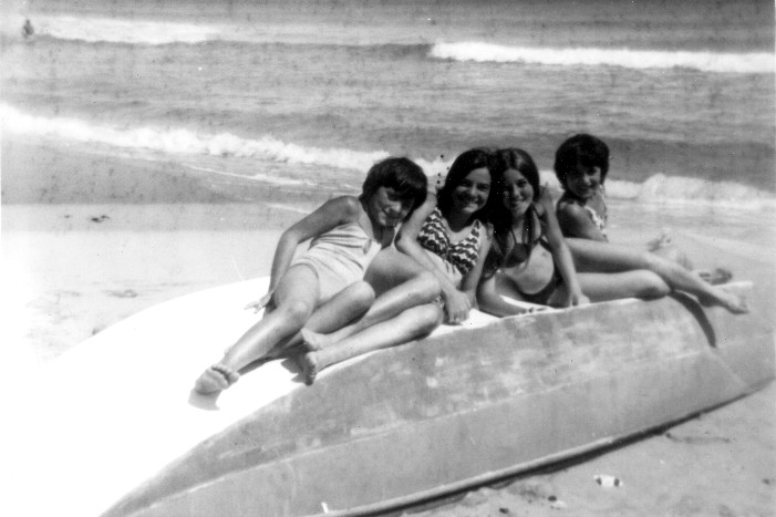 four women sit on the end of a surf board at the beach