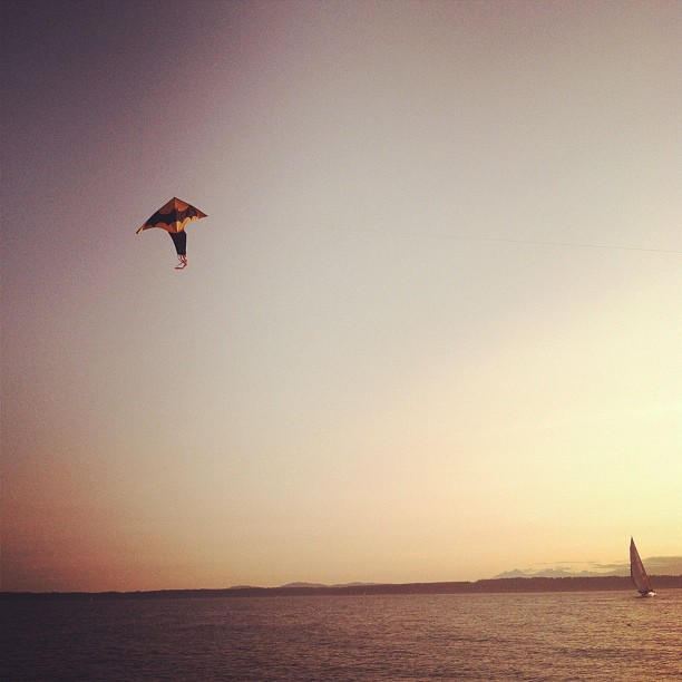 a kite flies high above the ocean during sunset