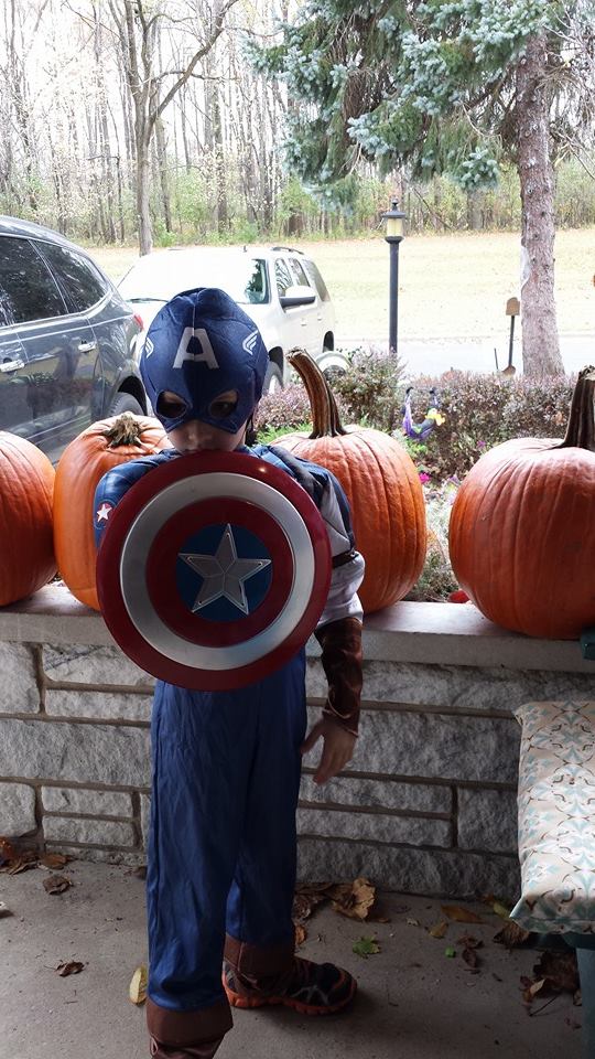 a boy dressed up as captain america with pumpkins on the side of the street