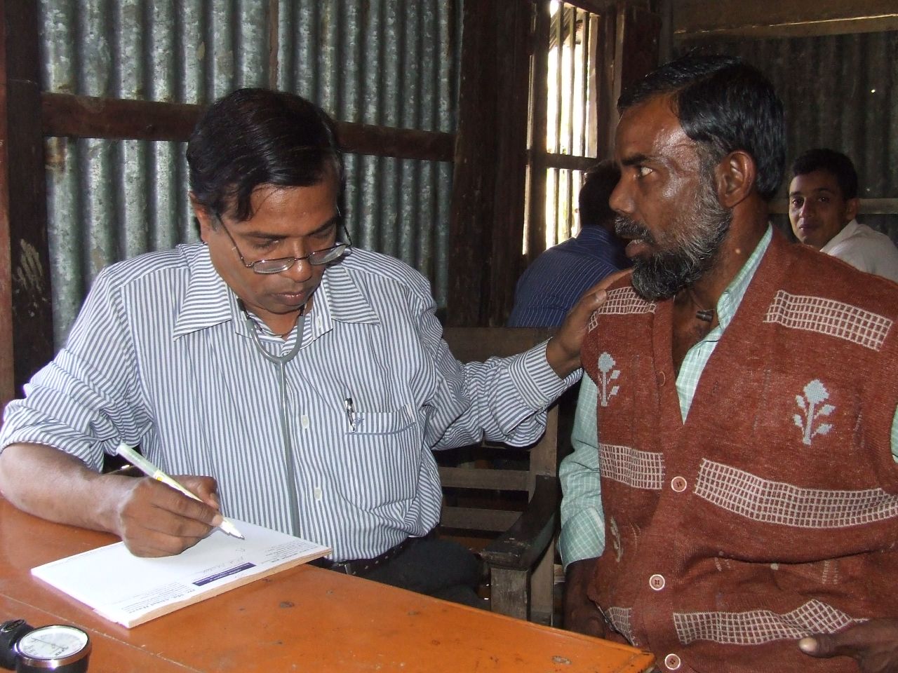 a man reading while another mans writes on his desk