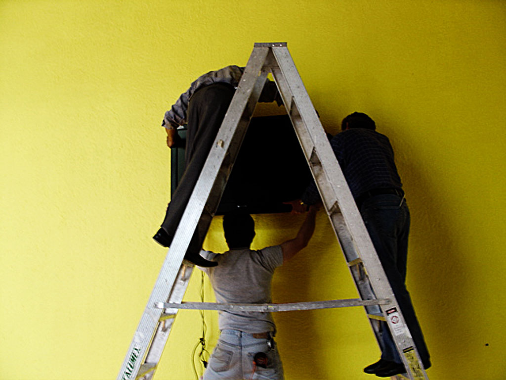 two people on ladders painting a yellow wall