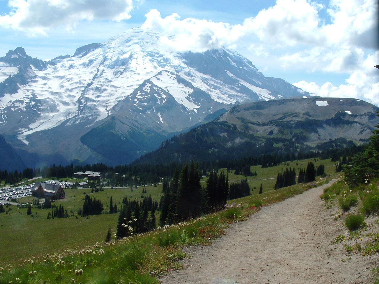 the path runs along side of a grassy area and past a snowy mountain