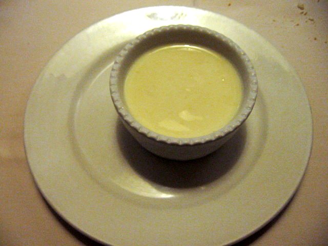 a white plate with a small bowl of yellow liquid on top