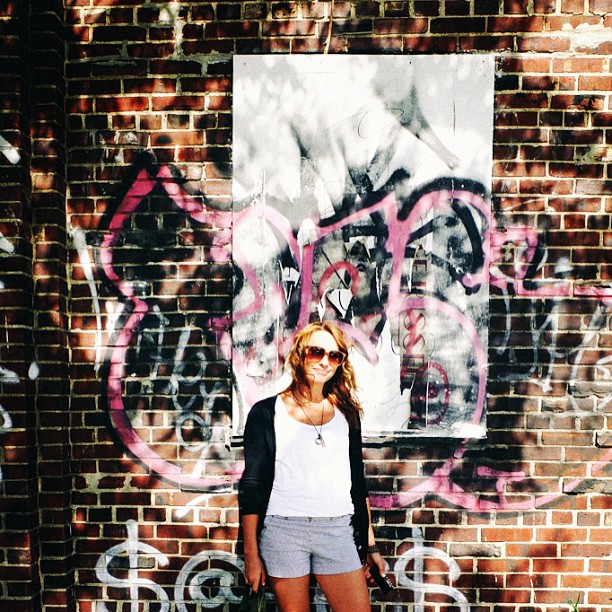 a woman in shorts standing in front of a wall with graffiti