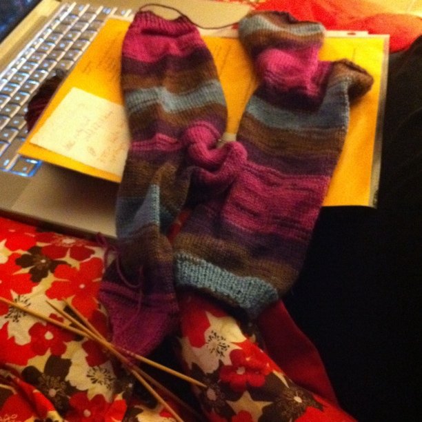 two knitted gloves sitting on top of blankets next to a laptop