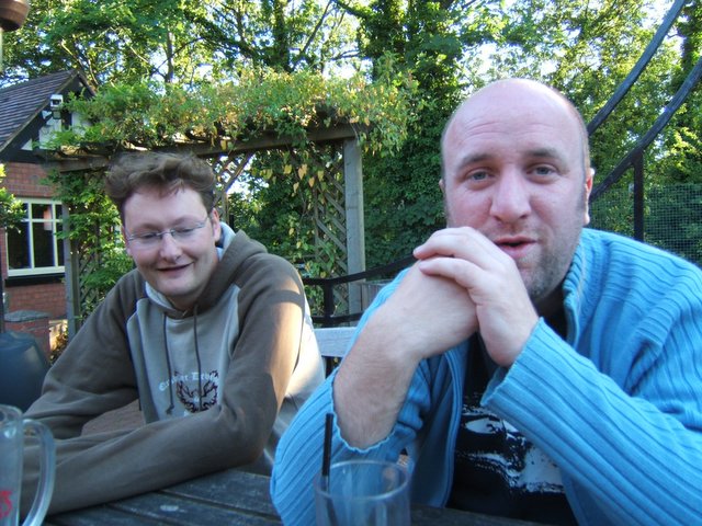 two men sitting at a table with cups of drinks