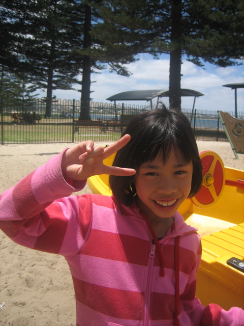 a small child making a hand gesture next to a playground