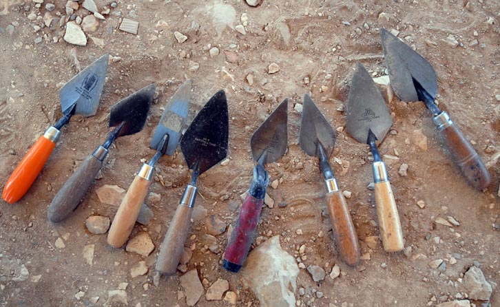 five pairs of gardening implements laid out on a sandy field