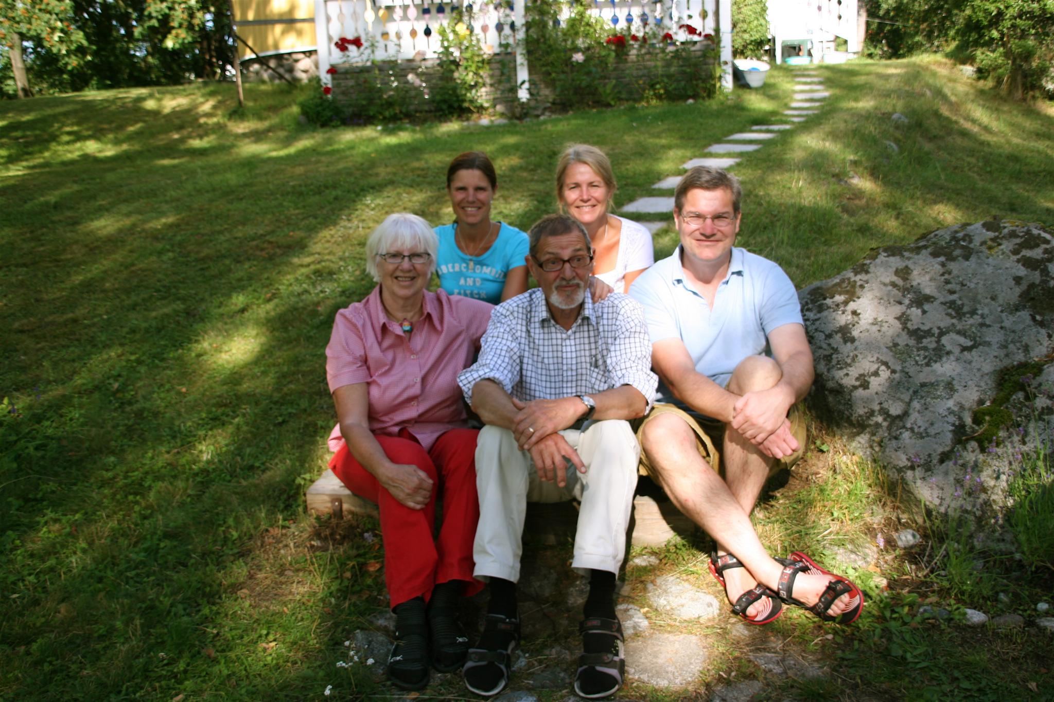 several people sitting on a rock in the grass near some trees