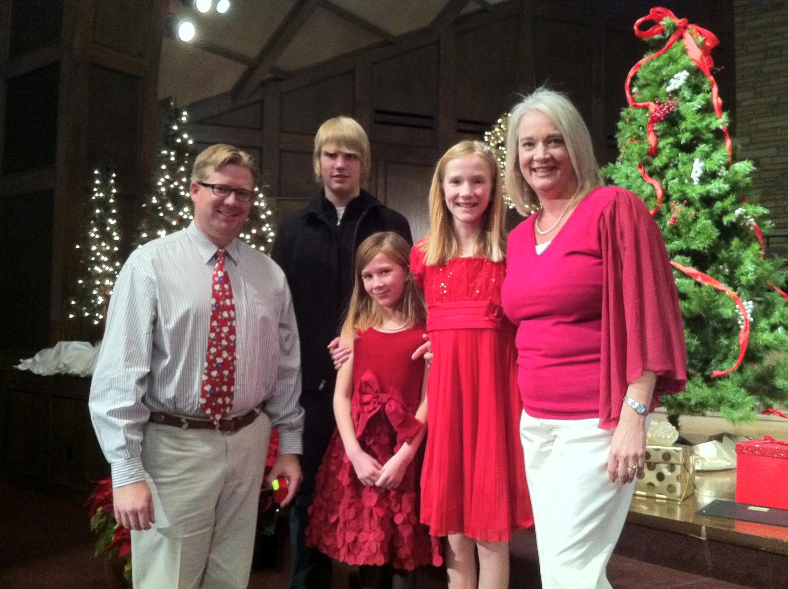 three men and a woman are posing for a picture in front of the christmas tree