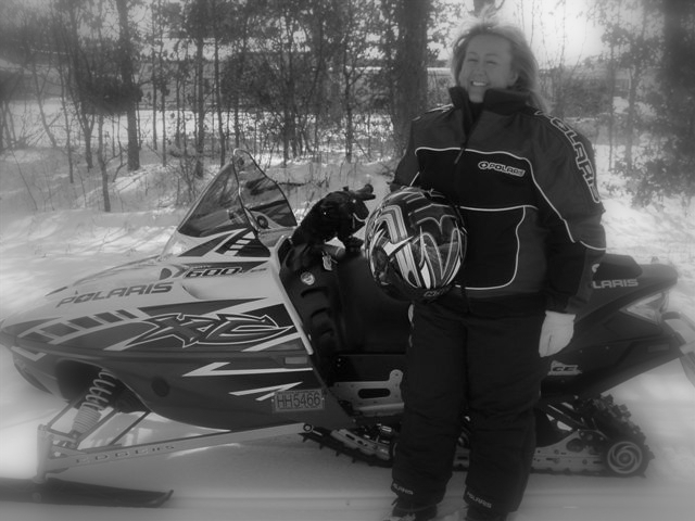 a woman stands next to her snowmobile and ski