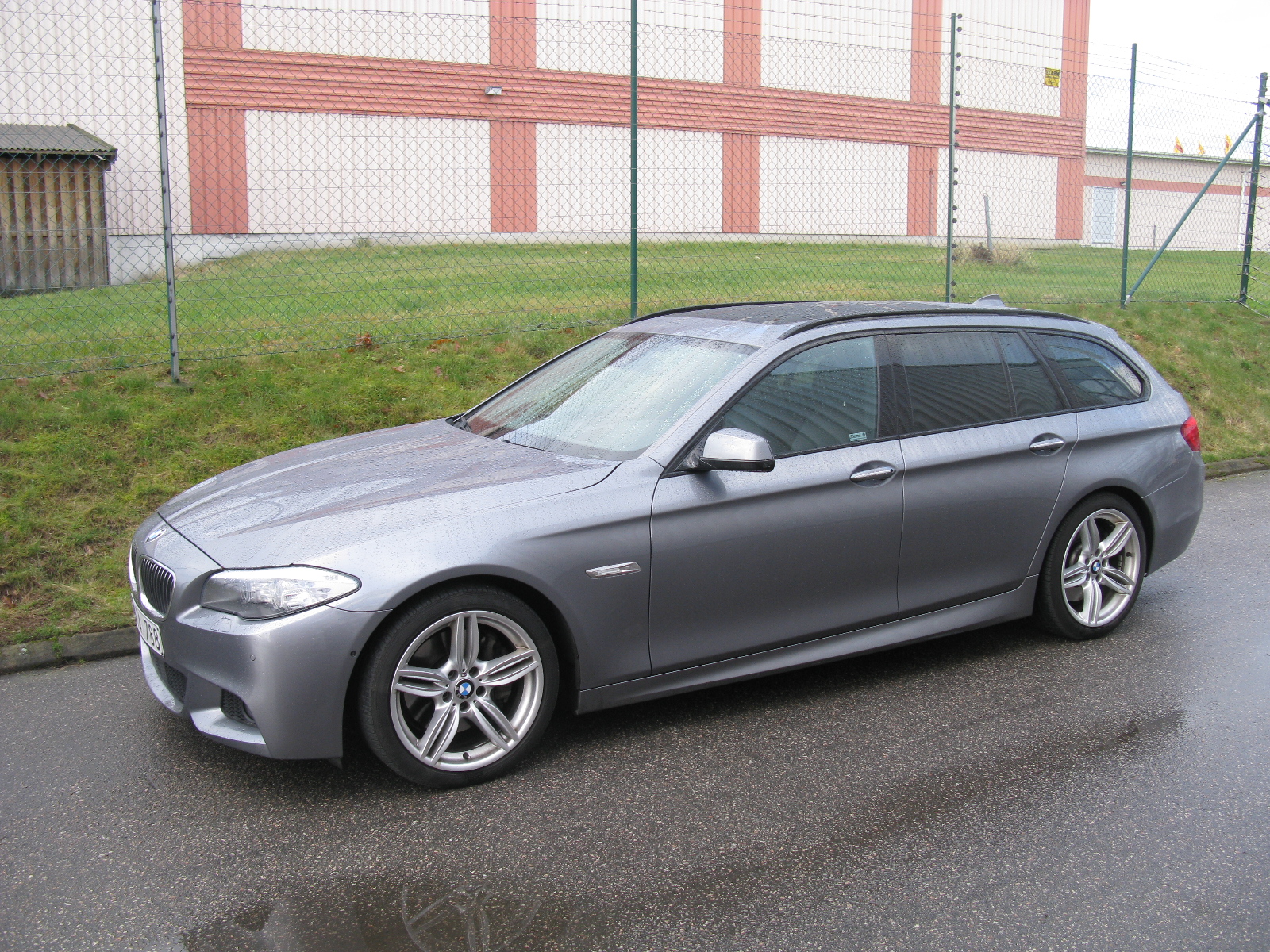 a bmw wagon sits parked in front of a fence