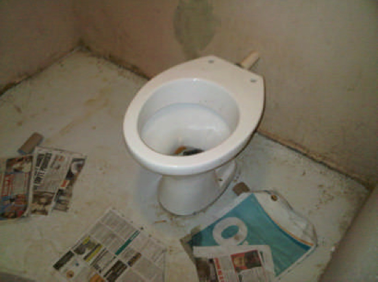 a toilet in a dirty stall with newspaper on the floor