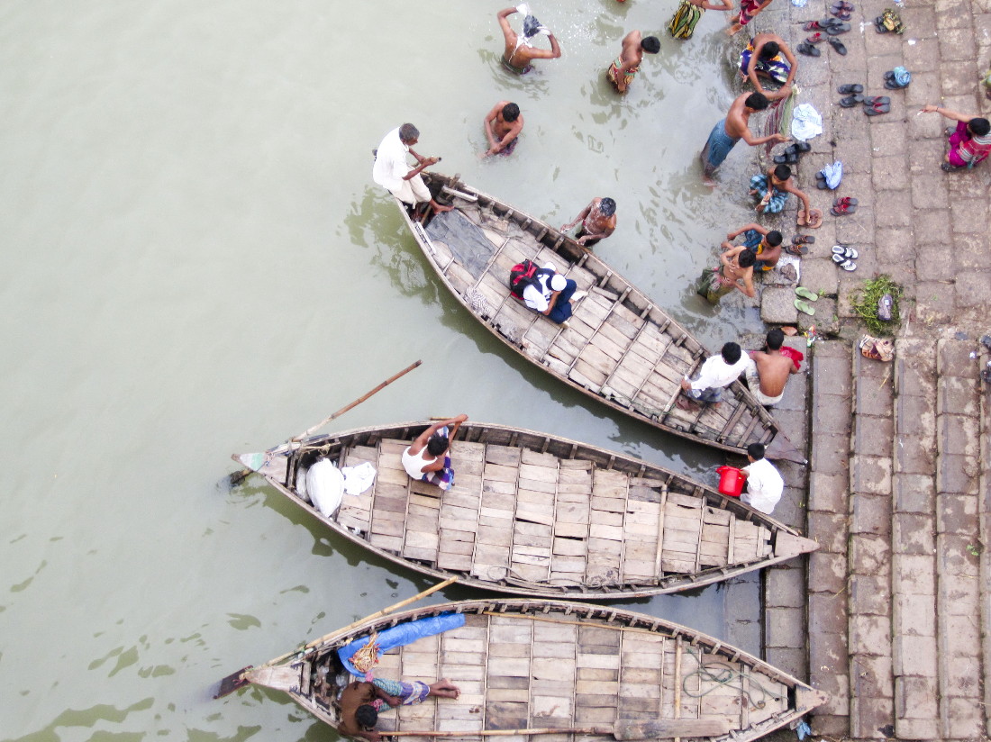 several boats parked on the river with people standing around them