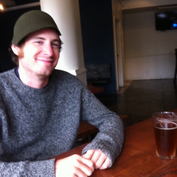 a smiling man sitting at a table with two glasses