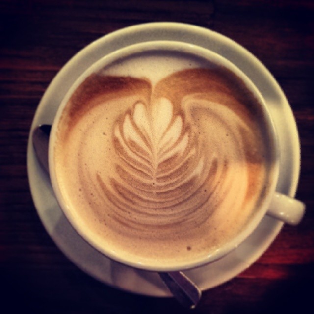 a white cup filled with milk with leaves drawn on it