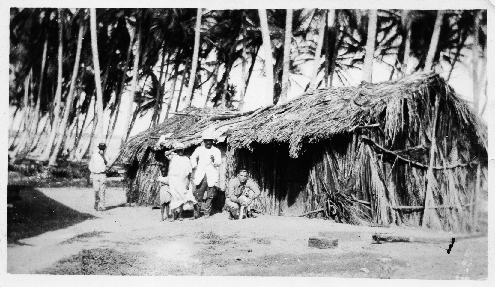 men standing in front of a hut under palm trees