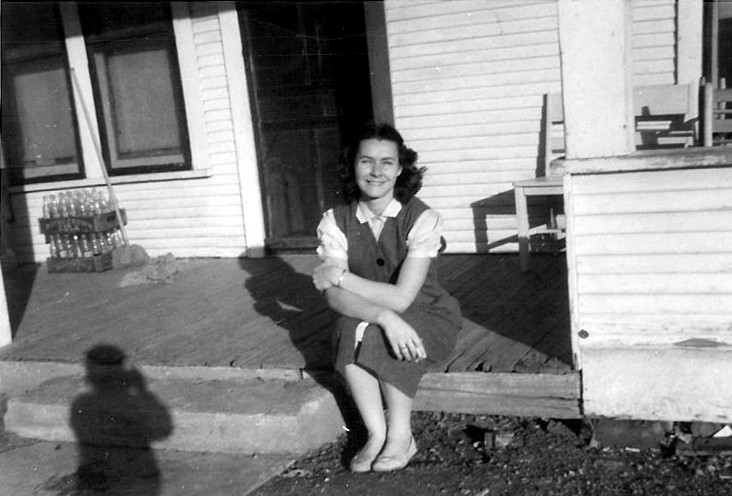 an old picture of a woman sitting on the porch of her home