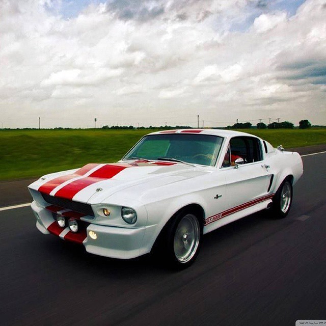 a white mustang driving down the road on a partly cloudy day