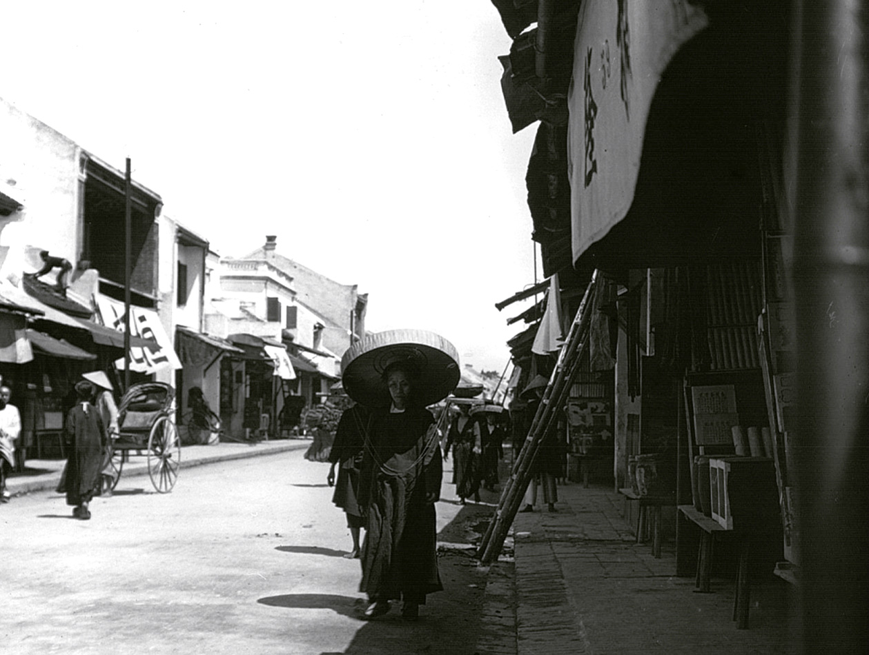 an asian woman with her shopping cart and her parasol walks down the street in an old town