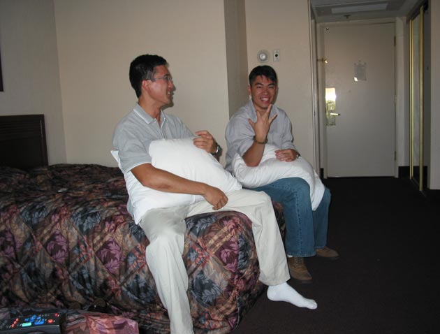 two men sitting on top of a bed talking and laughing