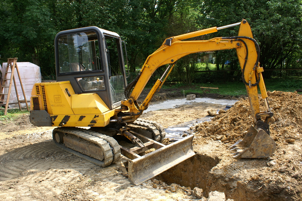 an excavator digging earth around trees with it's doors open