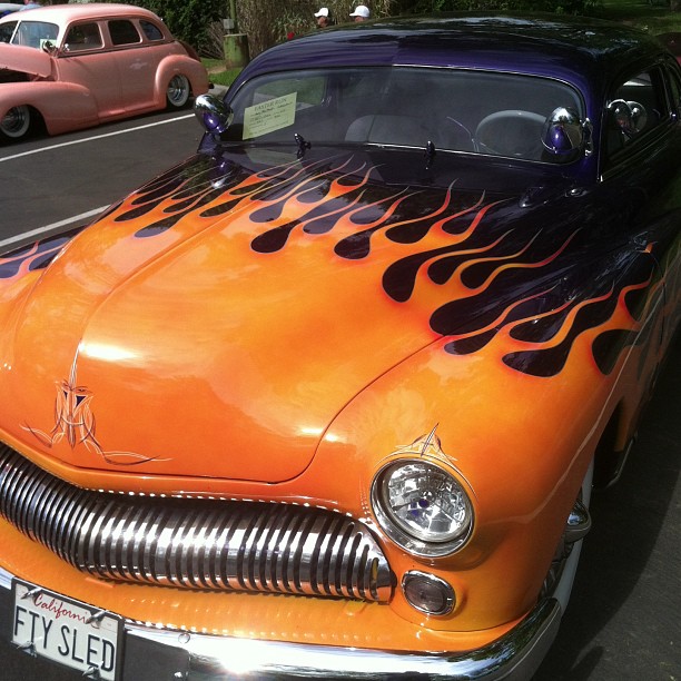 an orange car with flame and black hood sitting in a parking lot