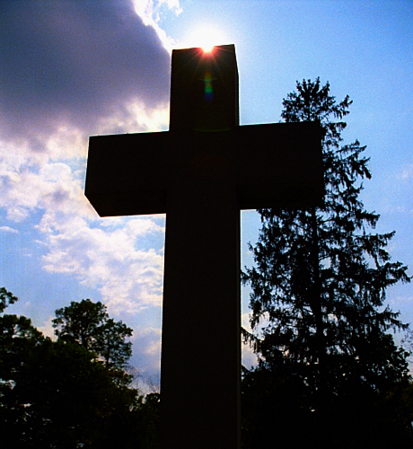 a cross and sun shines through clouds above