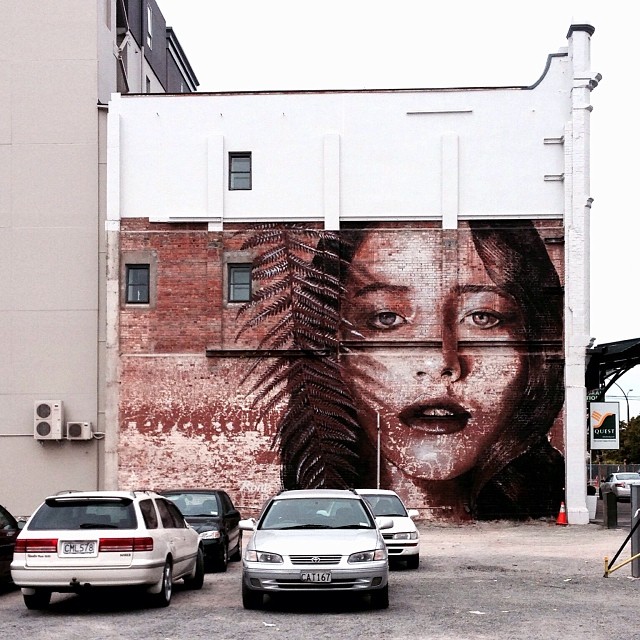 cars parked by a wall painted with the image of a woman