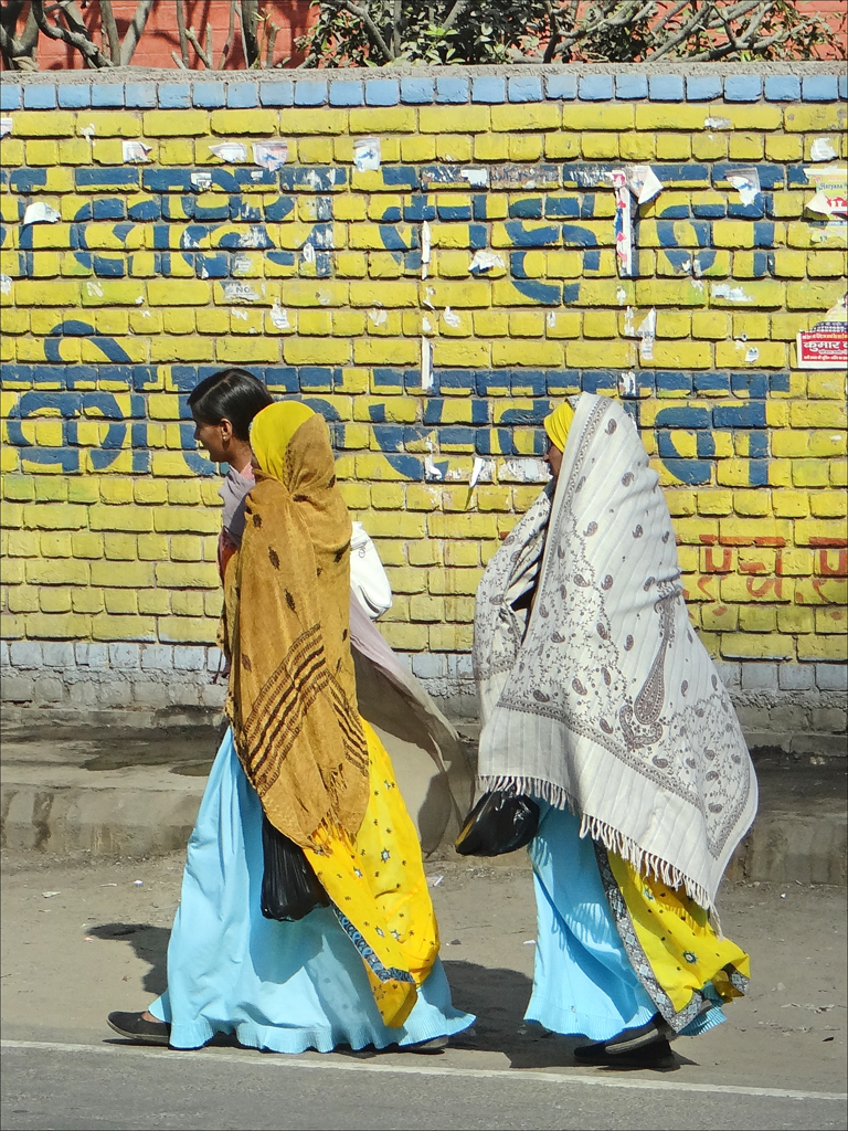 two women in brightly colored dresses walking by the wall