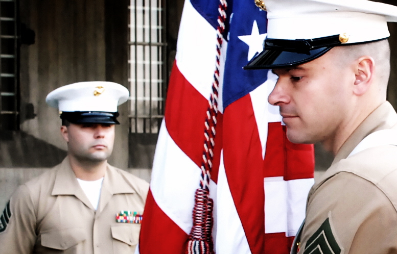 two military men stand next to an american flag