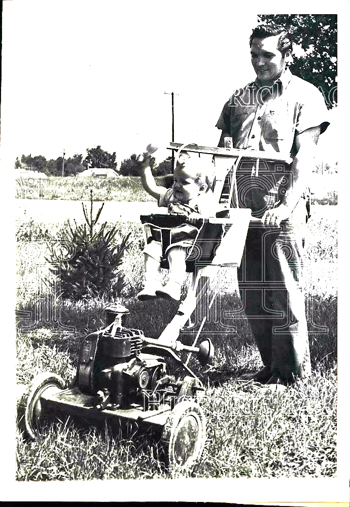 a black and white pograph shows a man operating a lawnmower