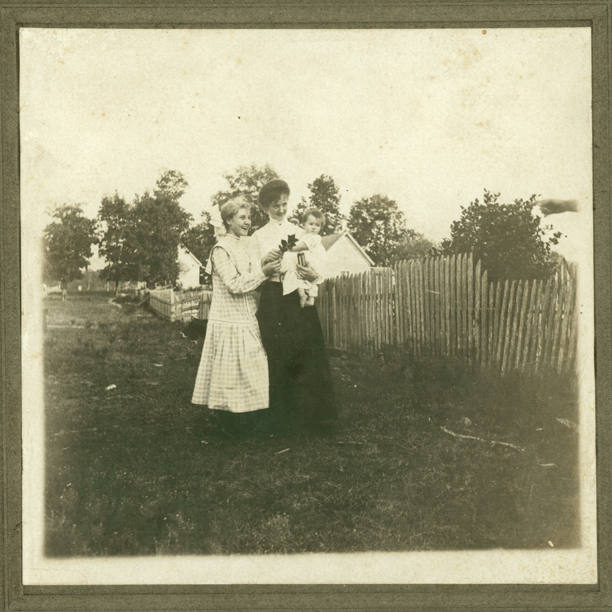 two women stand outside near a fence in the yard