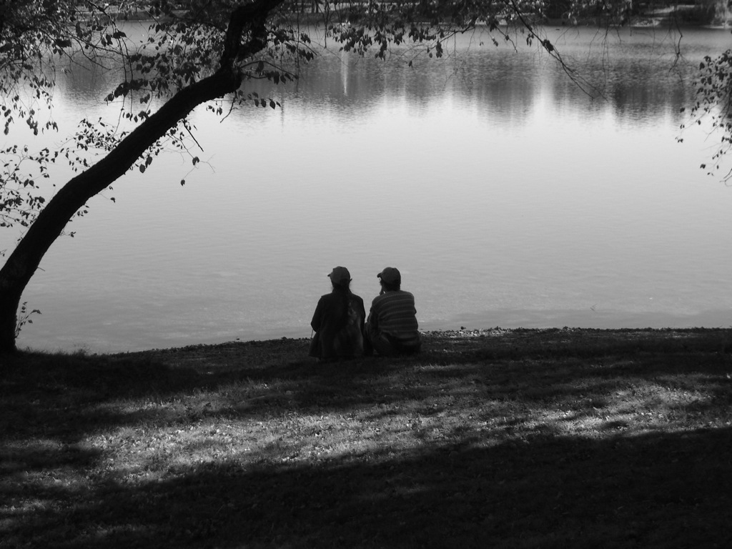 two people sit in front of a body of water