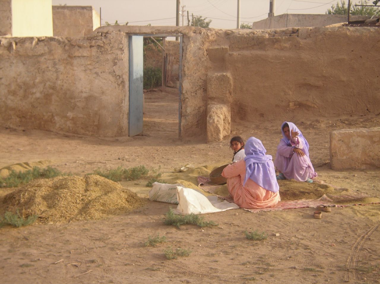 two girls sitting by a house next to an area with sand