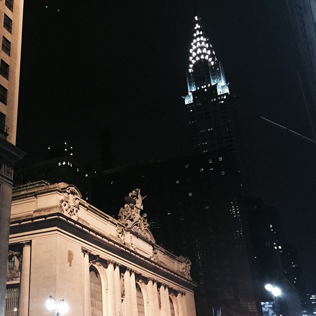 an illuminated clock tower stands above a city street